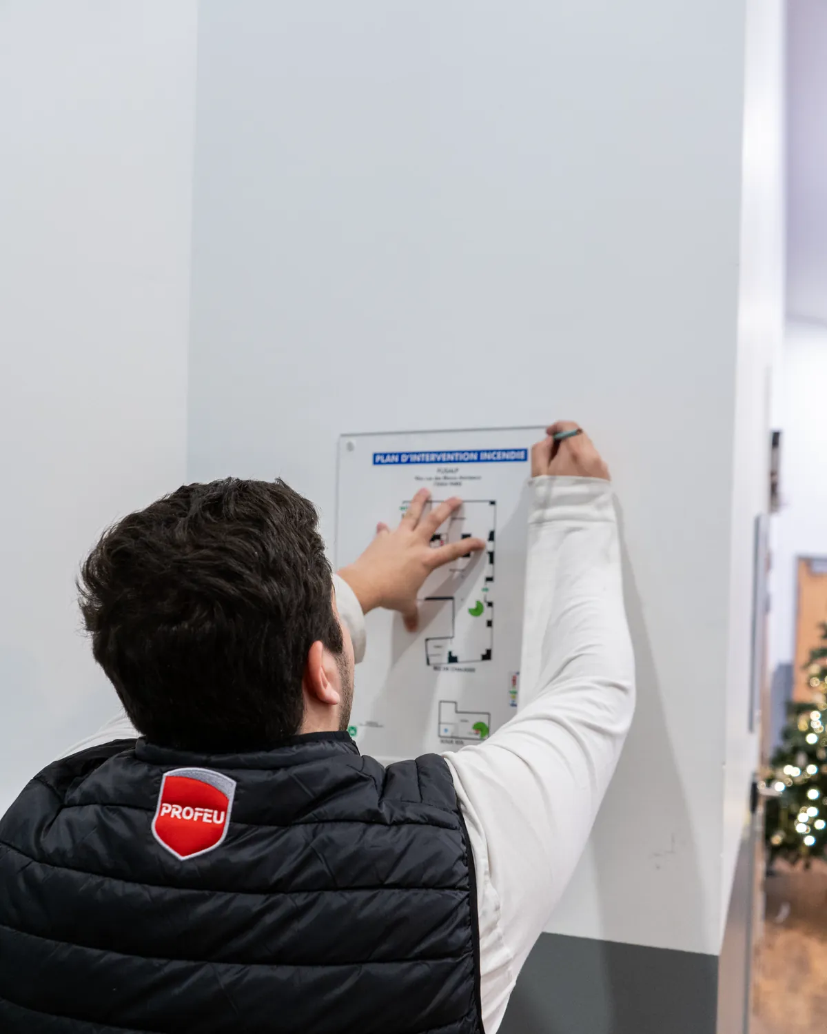Technicien PROFEU complétant un plan d'intervention incendie affiché au mur d'un couloir